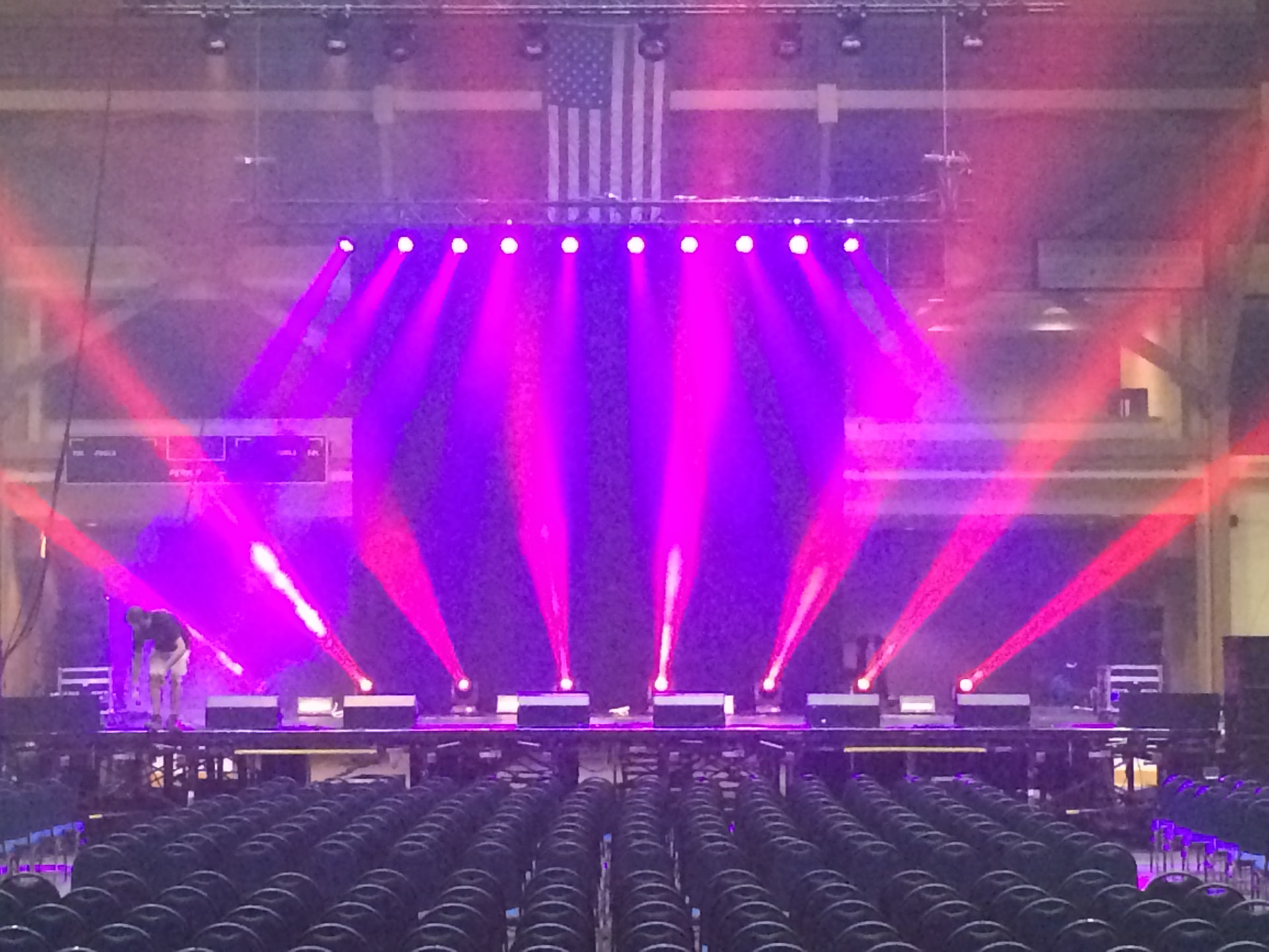 Arena stage washed in magenta and red beams over rows of seating